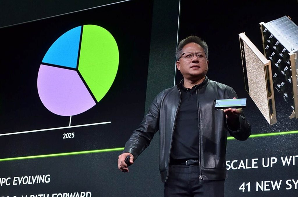 Jensen Huang holding a small computer component, standing in front of graphs